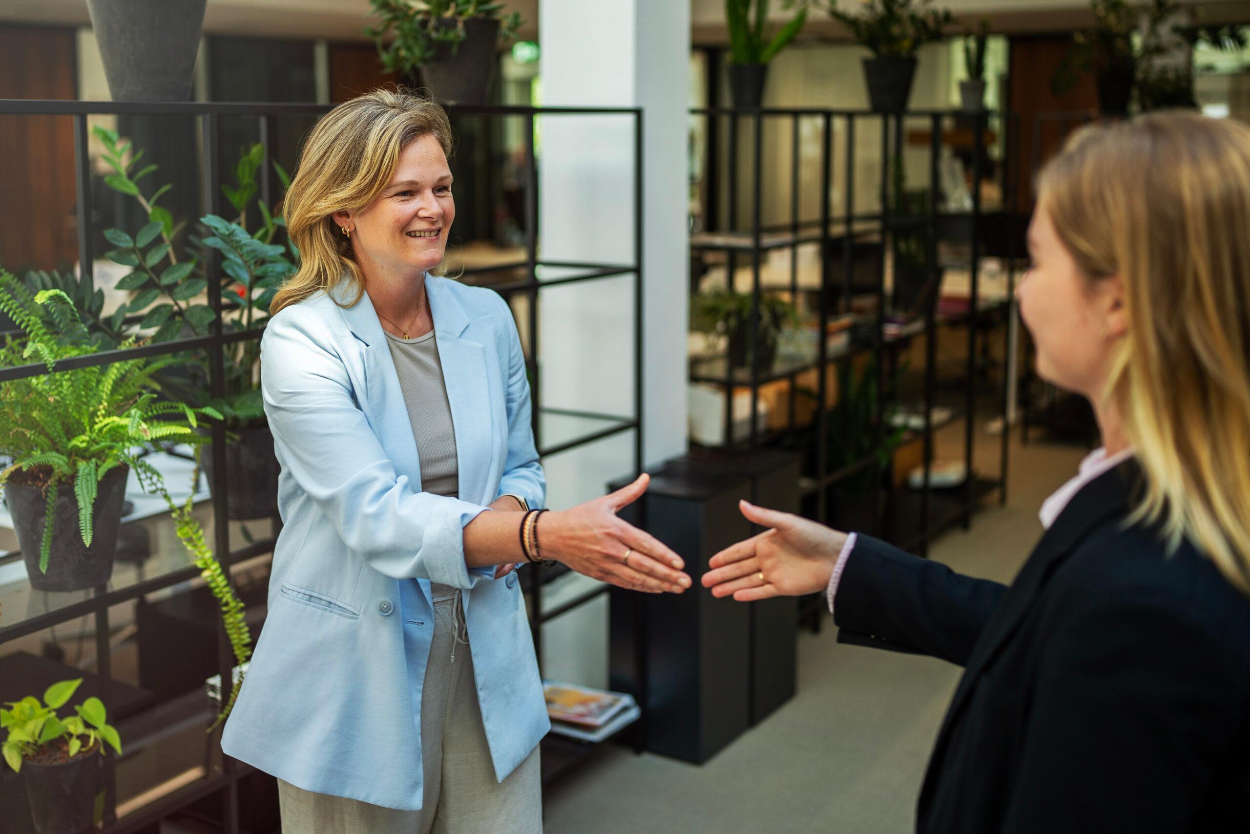 Een HR manager schudt de hand van een sollicitant waarmee ze een sollicitatiegesprek heeft gevoerd.