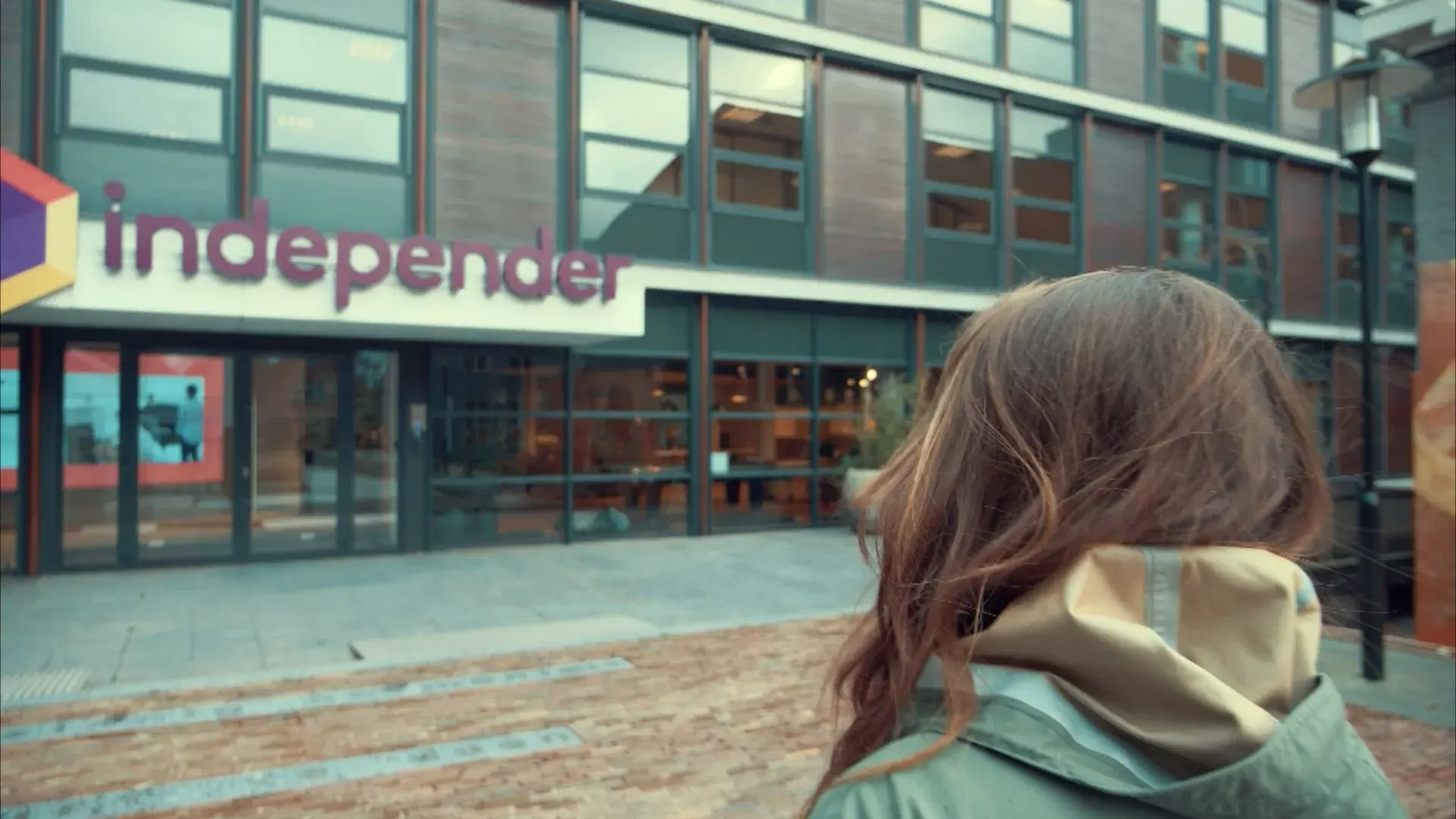 Jonge vrouw loopt richting het moderne gebouw van Independer in Hillywood onderstreept de dynamische en inspirerende werkomgeving